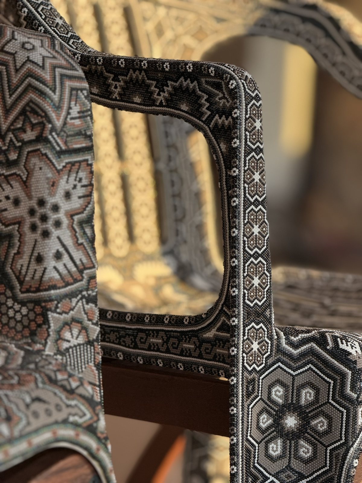 The beaded armrest frame of CHAQUIRA, with flower and star patterns in black, white and grey glass beads