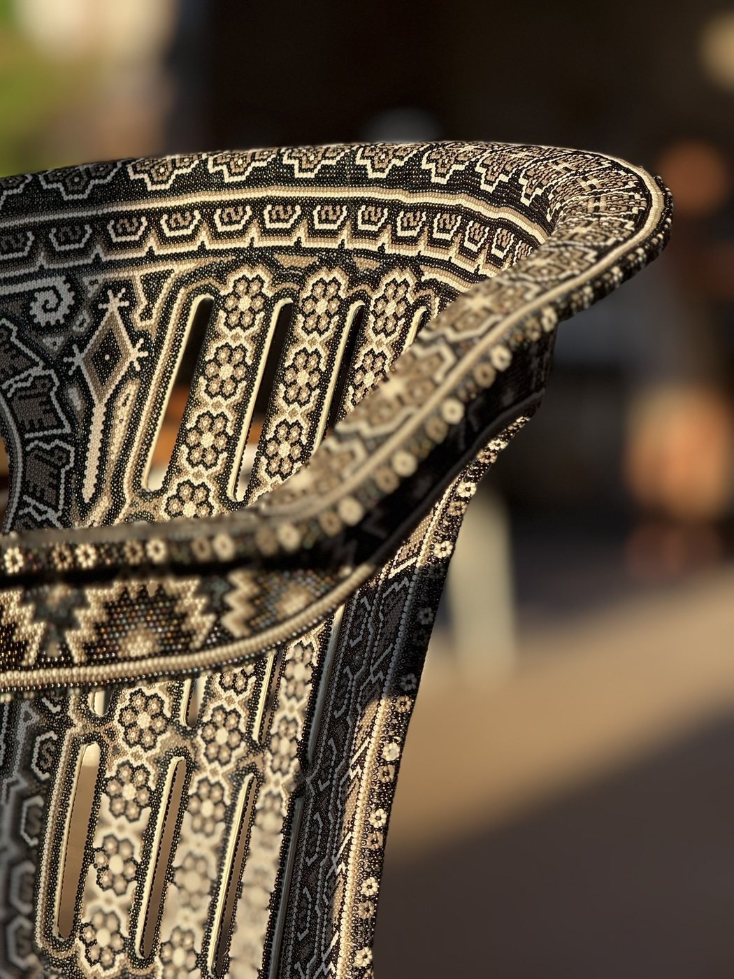 Close-up of the CHAQUIRA backrest and armrest in warm light: black, white and iridescent glass beads in Wixárika flower and step patterns