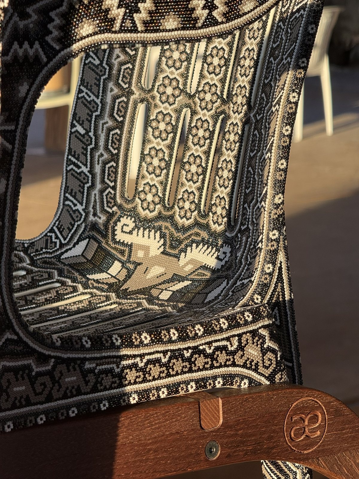 CHAQUIRA's beaded seat and backrest in warm sunlight, resting on the oak rocker with its carved æ