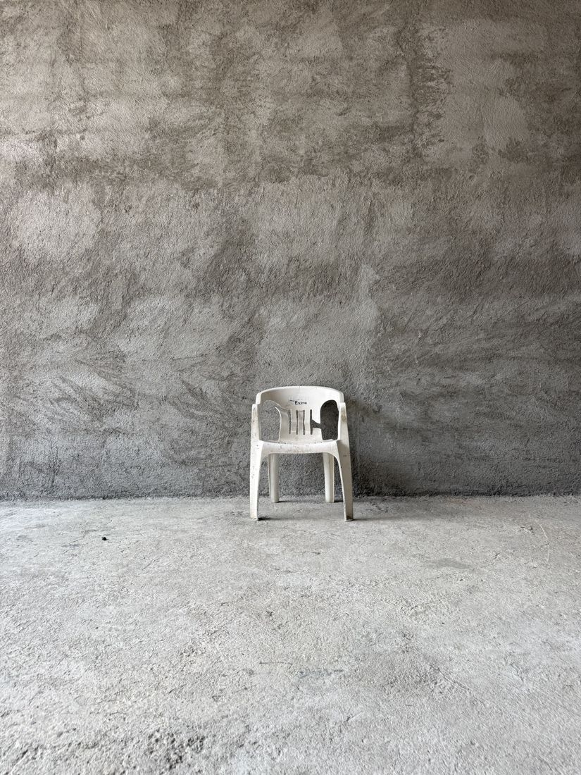 A lone white monobloc with the word Extra on its back, against a rough plaster wall