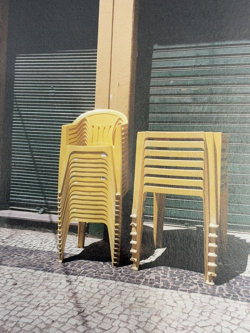 Two stacks of yellow chairs in front of a shuttered shop